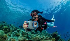 Subacquea in immersione con custodia Sealife SportDiver S per smartphone, mentre fotografa una barriera corallina tropicale.