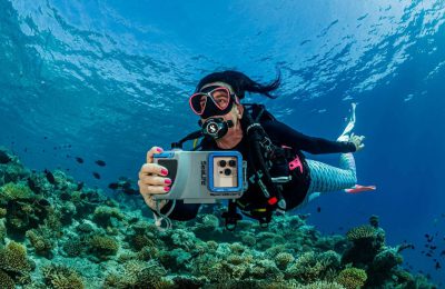 Subacquea in immersione con custodia Sealife SportDiver S per smartphone, mentre fotografa una barriera corallina tropicale.