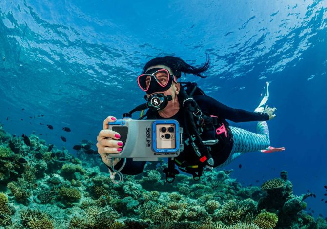 Subacquea in immersione con custodia Sealife SportDiver S per smartphone, mentre fotografa una barriera corallina tropicale.