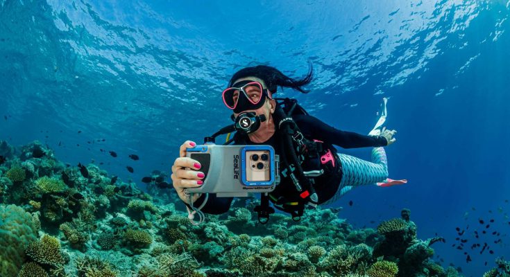 Subacquea in immersione con custodia Sealife SportDiver S per smartphone, mentre fotografa una barriera corallina tropicale.