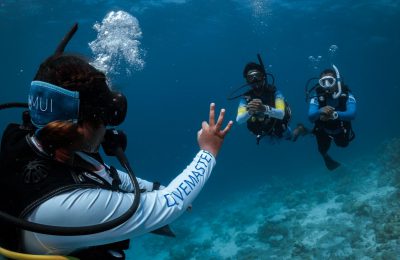 Divemaster PADI in immersione mostra il segnale OK a due subacquei: sicurezza e guida esperta durante una vacanza subacquea.