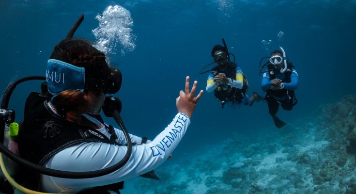 Divemaster PADI in immersione mostra il segnale OK a due subacquei: sicurezza e guida esperta durante una vacanza subacquea.