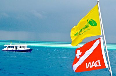 Bandiere Albatros Top Boat e DAN sventolano in navigazione alle Maldive, con dhoni sullo sfondo e reef degli atolli centrali crociera natale maldive subacquea