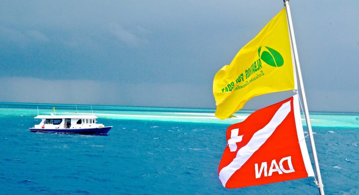 Bandiere Albatros Top Boat e DAN sventolano in navigazione alle Maldive, con dhoni sullo sfondo e reef degli atolli centrali crociera natale maldive subacquea