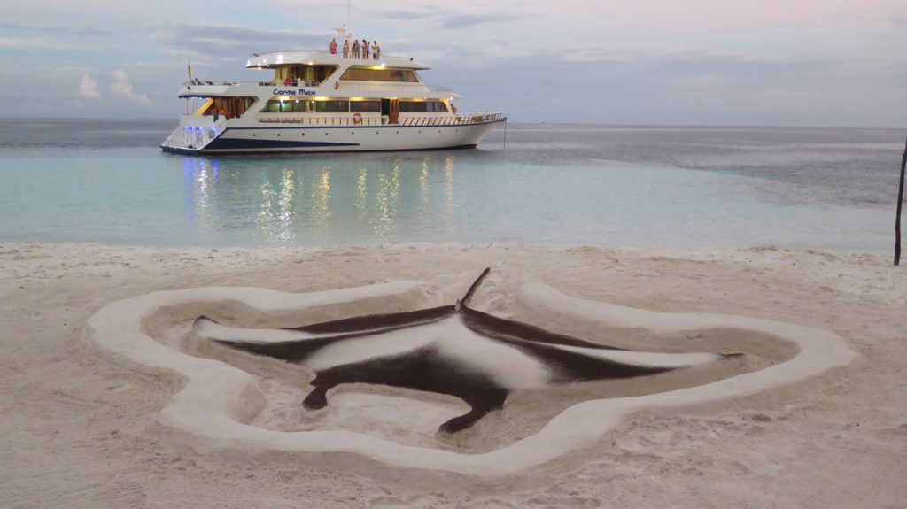 Yacht Conte Max alle Maldive, ancorato vicino a una spiaggia con scultura di manta nella sabbia. crociera subacquea maldive