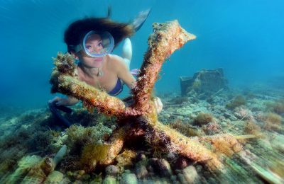 Donna in snorkeling osserva un’ancora ricoperta di organismi marini sul fondale costiero