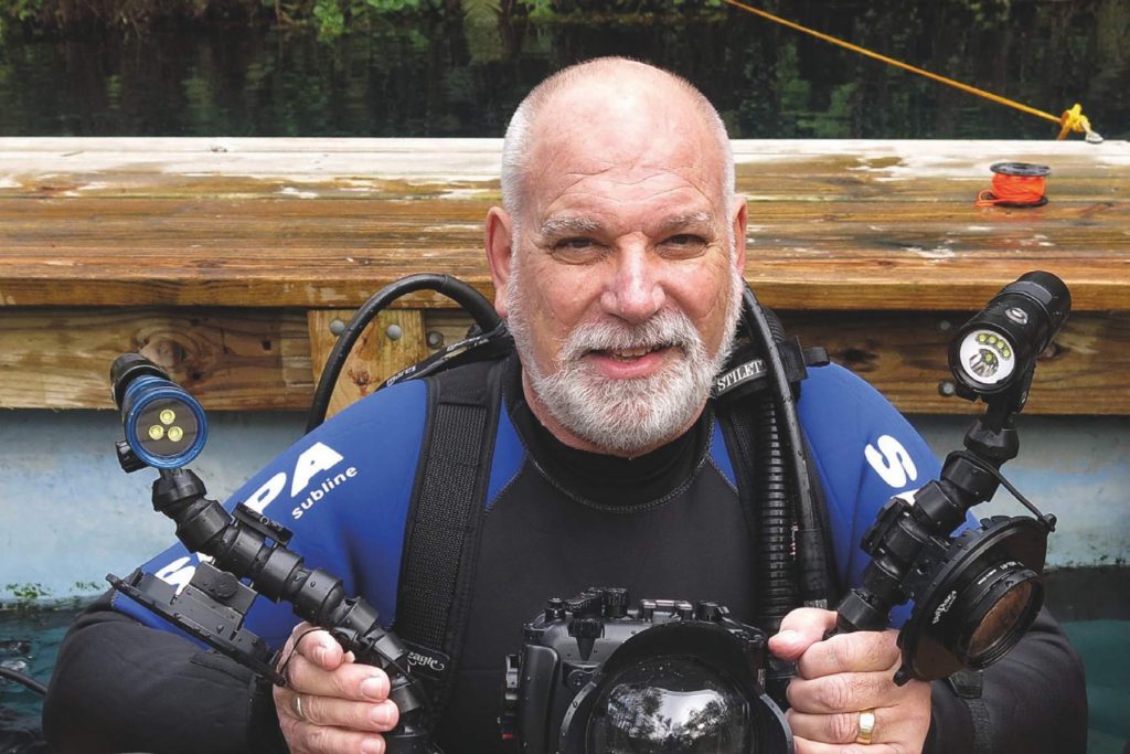 Howard Rosenstein in tenuta da immersione con attrezzatura fotografica subacquea, simbolo della sua carriera dedicata alla nascita della subacquea nel Mar Rosso.