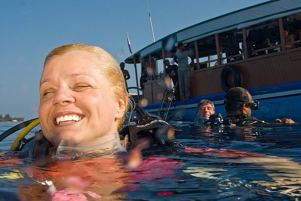 Primo piano di una donna subacquea felice e sorridente in superficie con maschera e muta. Benessere e subacquea.

