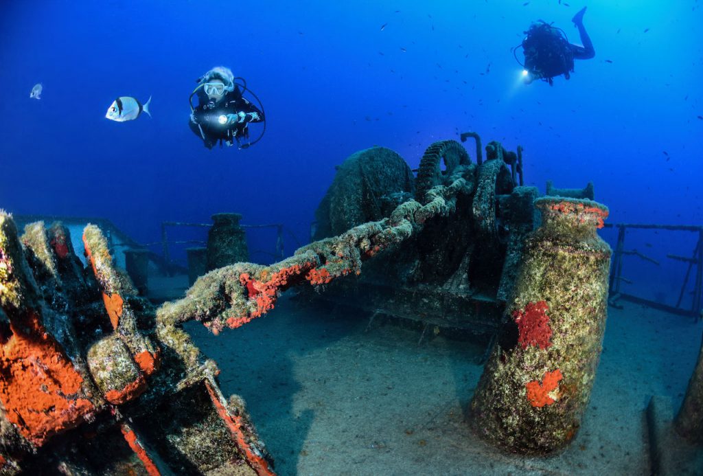 Subacquei esplorano l'interno del relitto Um El Faroud a Malta tra verricelli concrezionati e fauna marina