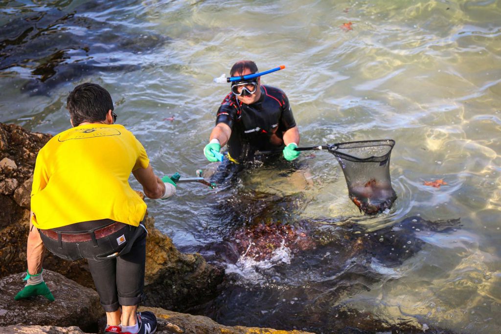 Un uomo in acqua consegna una rete piena di rifiuti a un altro uomo a riva