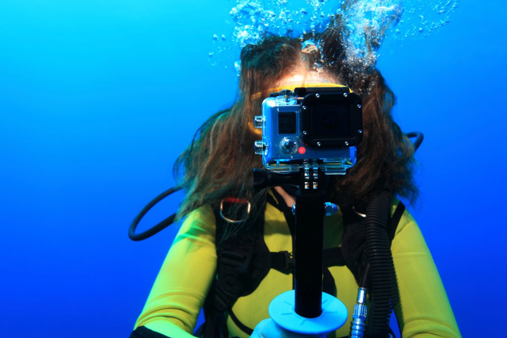 Giovane subacquea con una action cam durante un'immersione, mentre punta la fotocamera frontalmente.