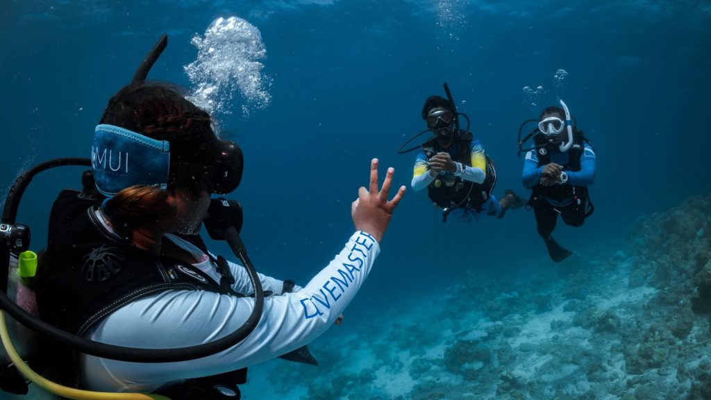 Divemaster PADI in immersione mostra il segnale OK a due subacquei: sicurezza e guida esperta durante una vacanza subacquea.