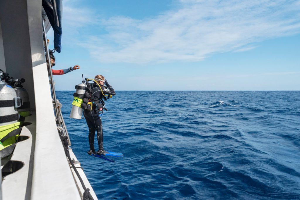 Subacqueo in ingresso in acqua da barca per immersione in corrente, con attrezzatura completa e mare aperto