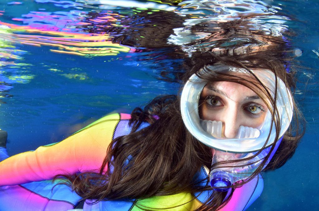 Ritratto subacqueo di una ragazza con maschera integrale e muta colorata durante snorkeling