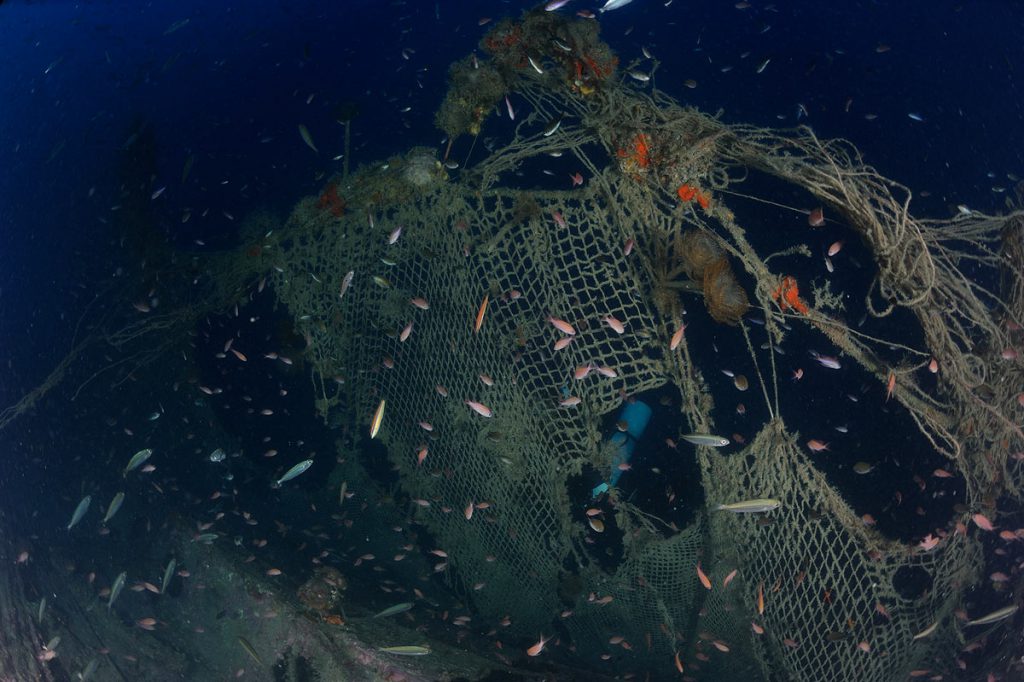 Reti fantasma avvolgono parte dello scafo del sommergibile Sebastiano Veniero, con coralli e banchi di pesci.