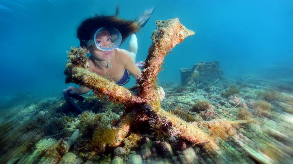 Donna in snorkeling osserva un’ancora ricoperta di organismi marini sul fondale costiero