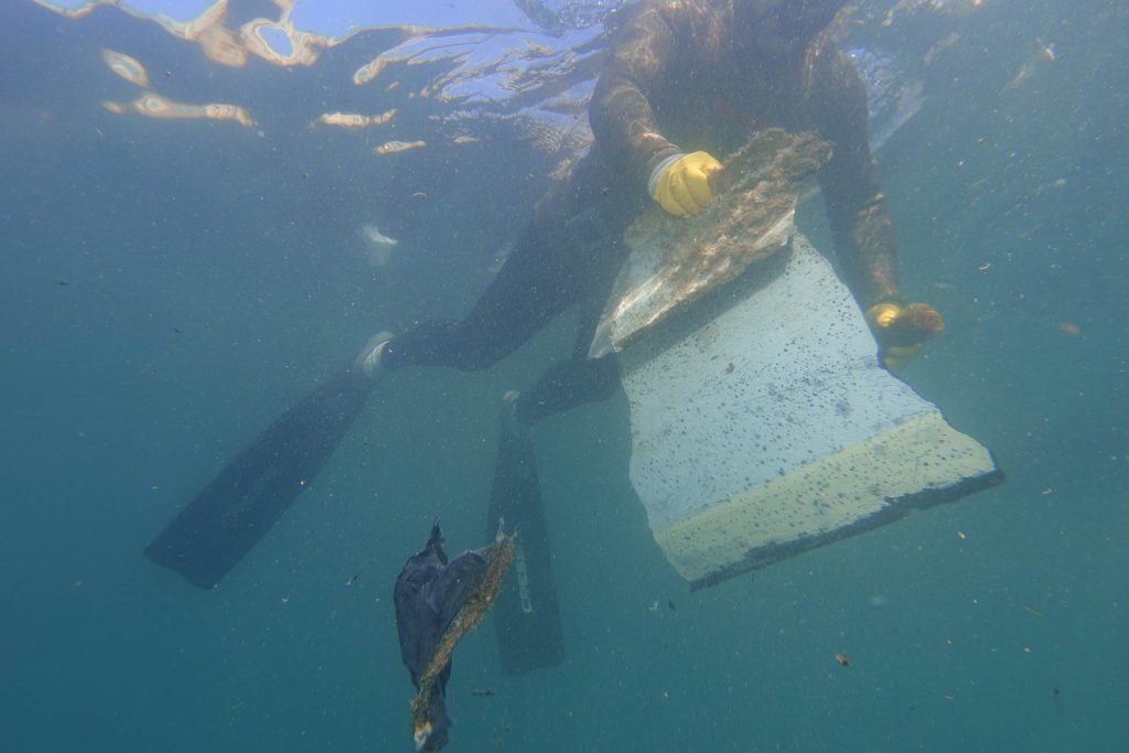 Fondali puliti: subacqueo che raccoglie un grande pezzo di polistirolo e un sacchetto di plastica dai fondali marini.