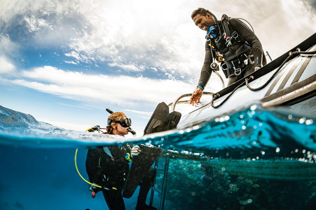 Corsi subacquei Padi: subacquea Padi che risale su una barca assistita da un istruttore.