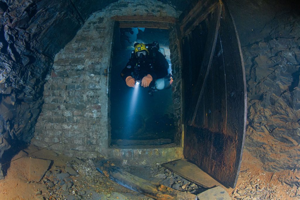 Subacqueo che osserva vecchie rotaie e strutture minerarie nella miniera di ardesia allagata di Nuttlar