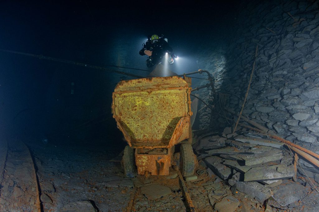 Subacqueo che illumina vecchie tubazioni industriali nella miniera di ardesia allagata di Nuttlar