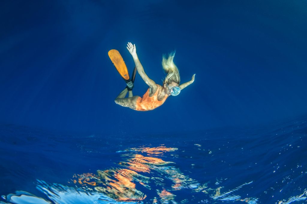 Apneista in discesa nel blu con riflesso della figura sulla superficie del mare