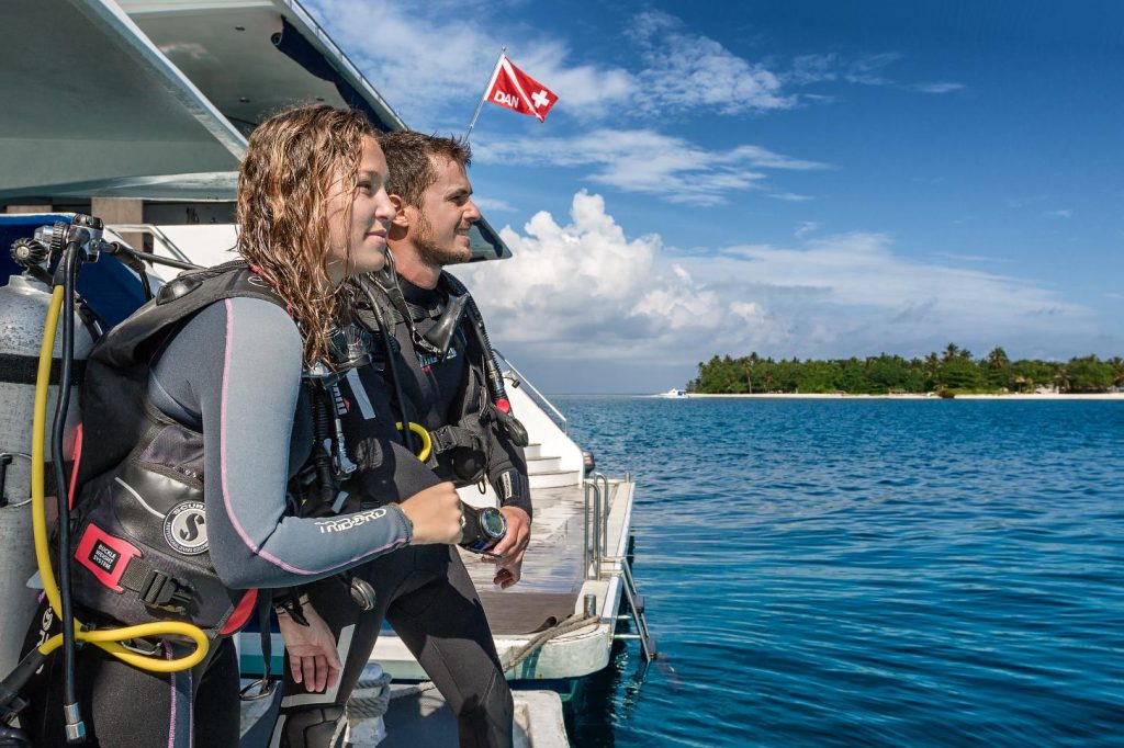 Subacquei pronti per l’immersione su una barca diving alle Maldive, con atollo sullo sfondo.