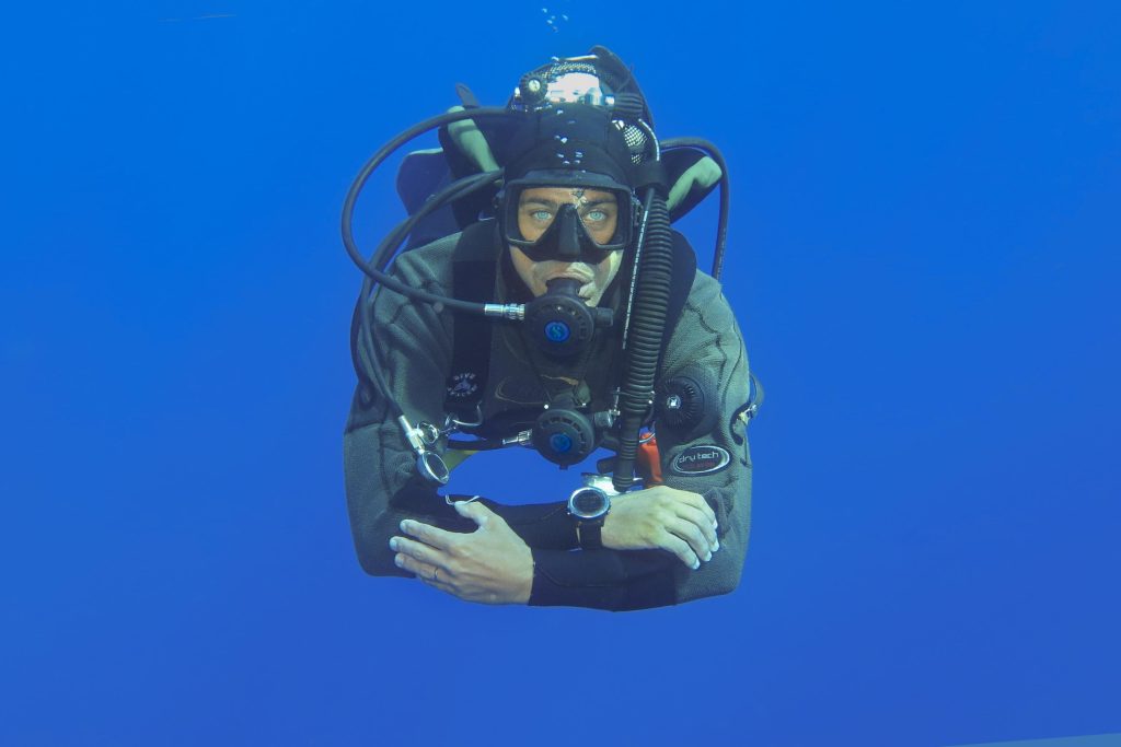 Ritratto frontale di subacqueo in immersione con attrezzatura tecnica su sfondo blu
